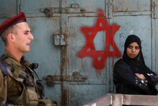 An Israeli soldier keeps guard near a Palestinian woman standing by a Star of David graffiti sprayed by Israeli settlers near an army checkpoint in the centre of the occupied West Bank city of Hebron on May 18, 2009 AFP